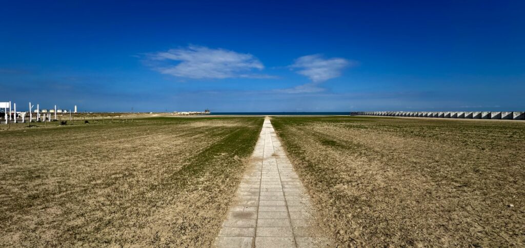 Küstenlandschaft mit einem geraden Weg zum Meer unter blauem Himmel
